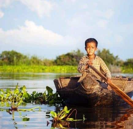 Cambodian boy travelling by boat in his floating village Cambodia